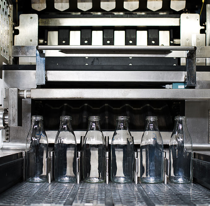 Ligne de production avec bouteilles en verre alignÃ©es sous une machine industrielle pour illustrer le rÃ©emploi des emballages