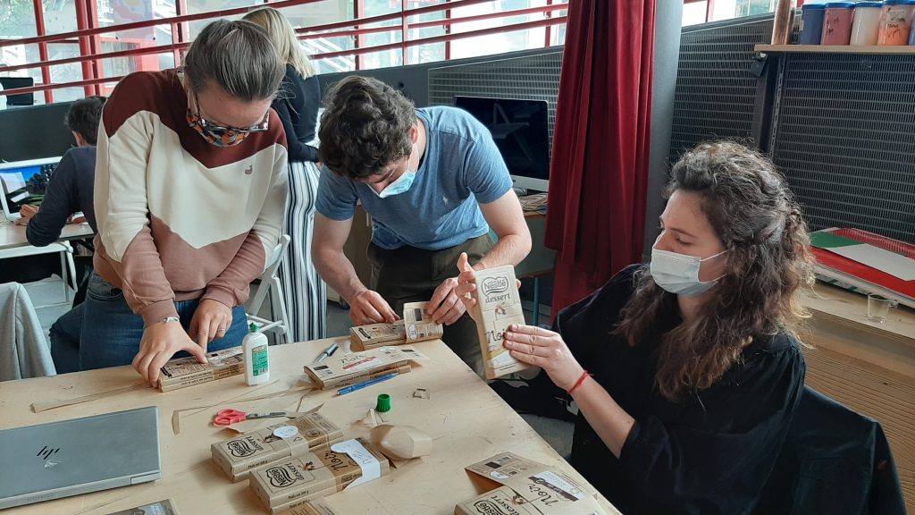 Trois personnes travaillent sur un prototype dâemballage utilisant un bandeau en papier kraft pour remplacer le film plastique autour des tablettes